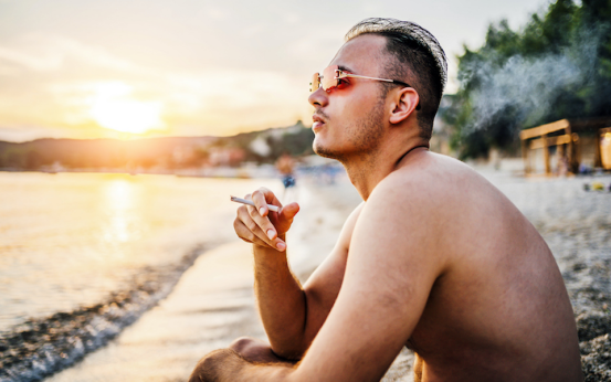 Man smokes with rolling paper on sunset beach.