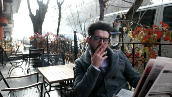 Person smoking with rolling paper (in an outdoor café setting, tied to premium rolling paper usage).