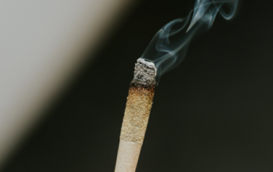 A lit cigarette with curling smoke, showing the ash formation that reveals rolling paper quality.
