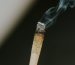 A lit cigarette with curling smoke, showing the ash formation that reveals rolling paper quality.
