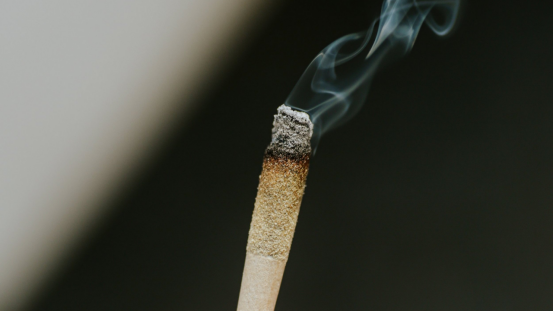A lit cigarette with curling smoke, showing the ash formation that reveals rolling paper quality.